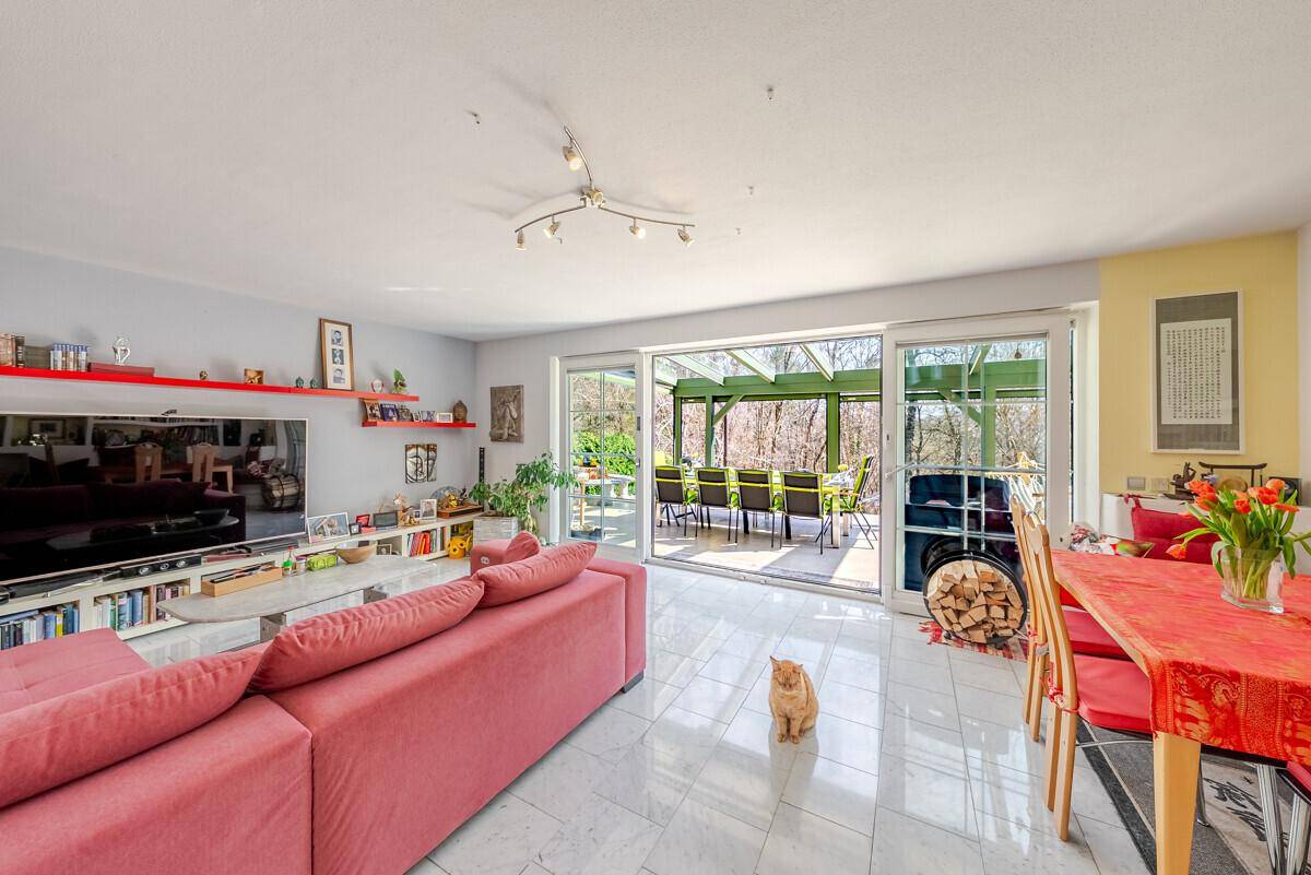 Gemütlicher Wohn-Essbereich mit Fliesenboden, rotem Sofa und Zugang zum Wintergarten.