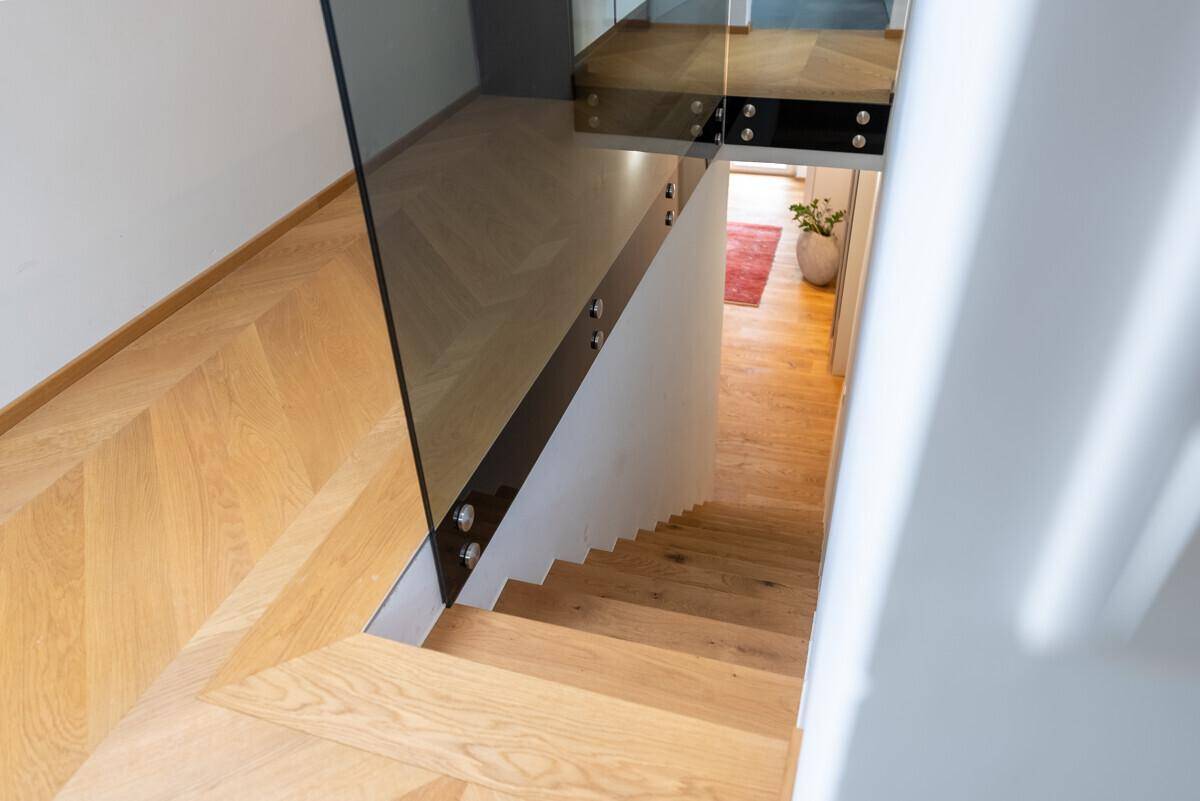 Moderne Holztreppe mit Glasgeländer, die verschiedene Ebenen des Hauses verbindet.