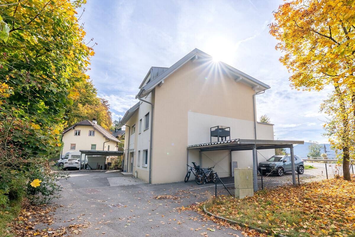 Mehrfamilienhaus mit Carports und herbstlicher Umgebung unter strahlendem Himmel.