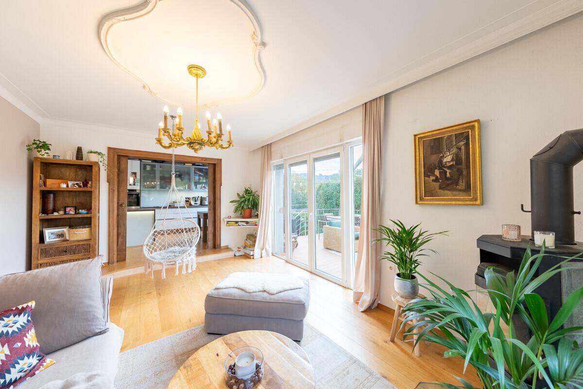 Helles Wohnzimmer mit Holzboden, Stuckdecke und Zugang zu einem Balkon mit Blick ins Grüne.