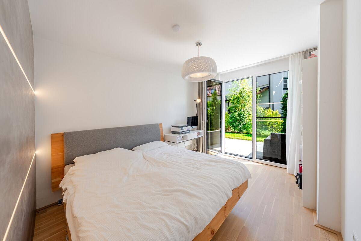 Helles Schlafzimmer mit Holzbett, großen Fenstern und direktem Zugang zur grünen Gartenfläche.