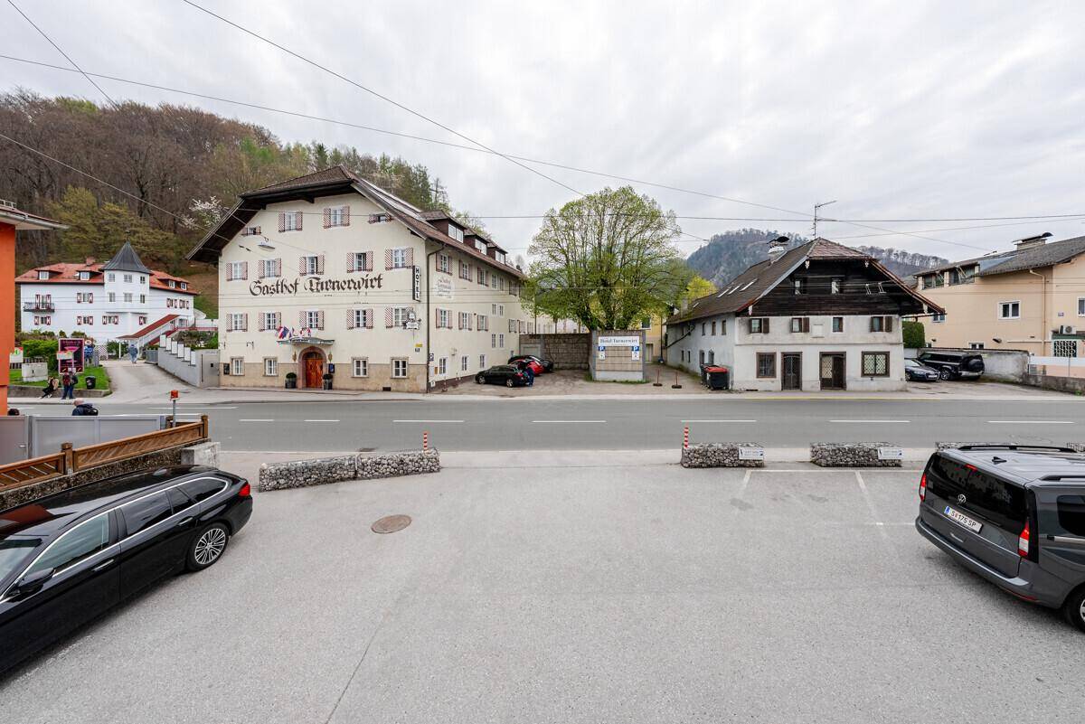 Straßenansicht mit traditionellen Gebäuden, Parkplätzen und bergiger Umgebung.