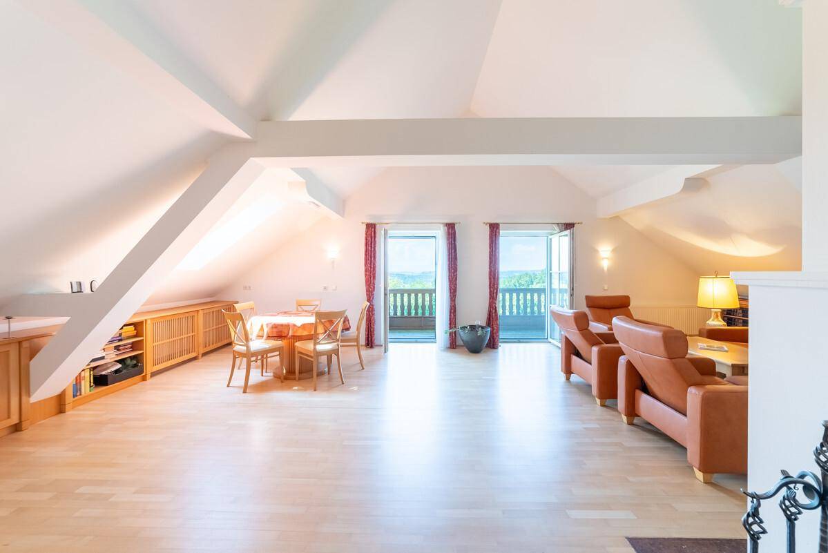 Helles Dachgeschoss mit offenem Wohn-Essbereich, Holzbalken und Zugang zu einem Balkon.