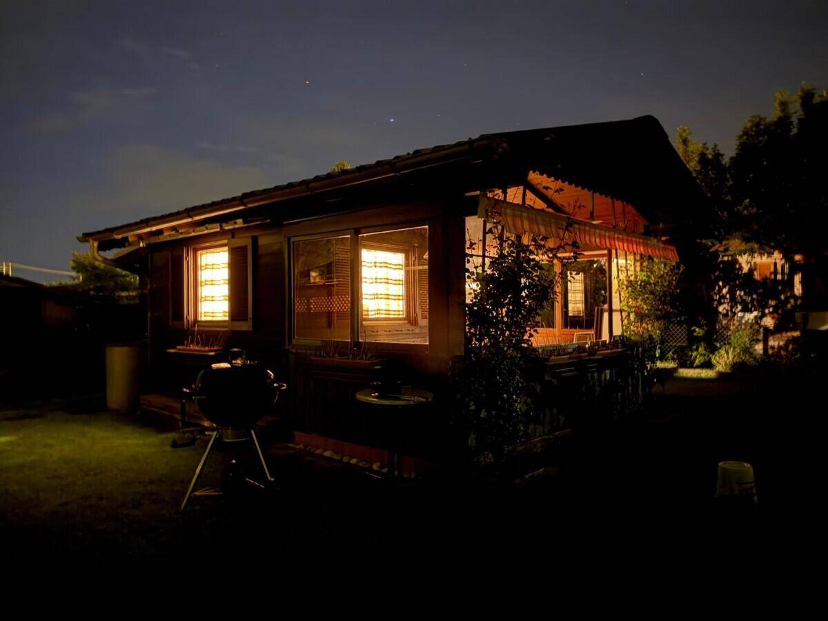Gemütliches Holzhaus bei Nacht mit beleuchteten Fenstern und einem Grill im Gartenbereich.