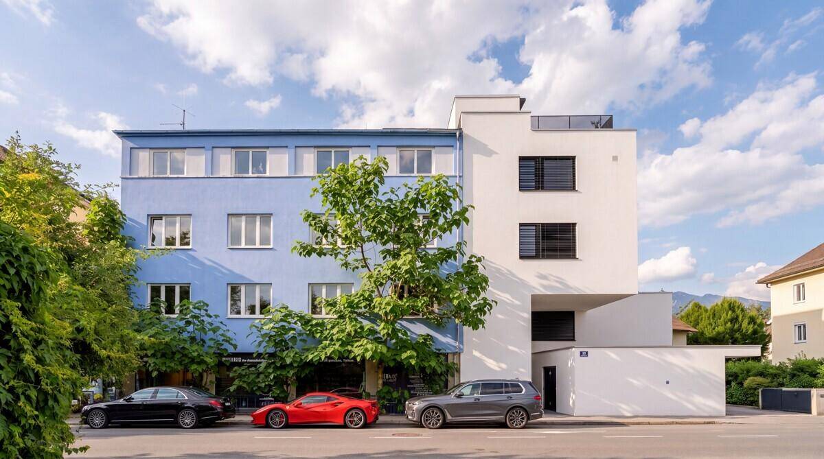Moderne Gebäudefassade mit blauen und weißen Abschnitten, großen Fenstern und parkenden Autos auf der Straße.