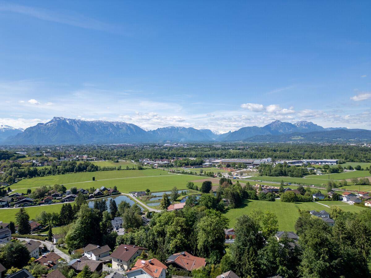 Panoramablick über eine weite Landschaft mit Siedlungen, Feldern, Seen und majestätischen Bergen.