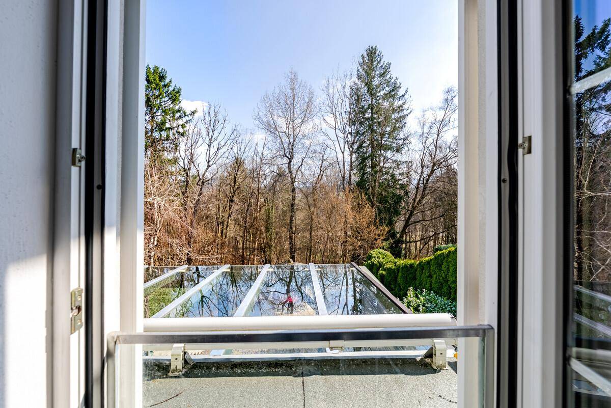 Blick aus dem Fenster auf den überdachten Wintergarten und die umliegenden Bäume.