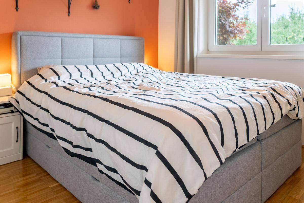 Gemütliches Schlafzimmer mit großem Doppelbett, farbiger Wand und Fenster mit Ausblick.