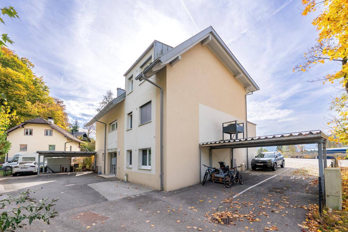 Ansicht des Gebäudes mit überdachten Stellplätzen und herbstlicher Bepflanzung.