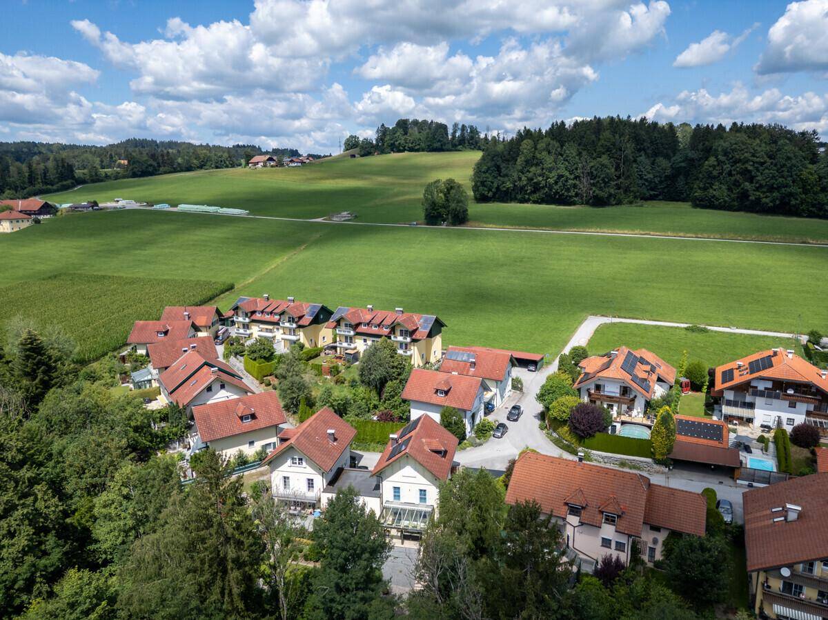 Weitläufige Luftaufnahme einer Wohnsiedlung am Rande eines Feldes mit grünen Hügeln im Hintergrund.
