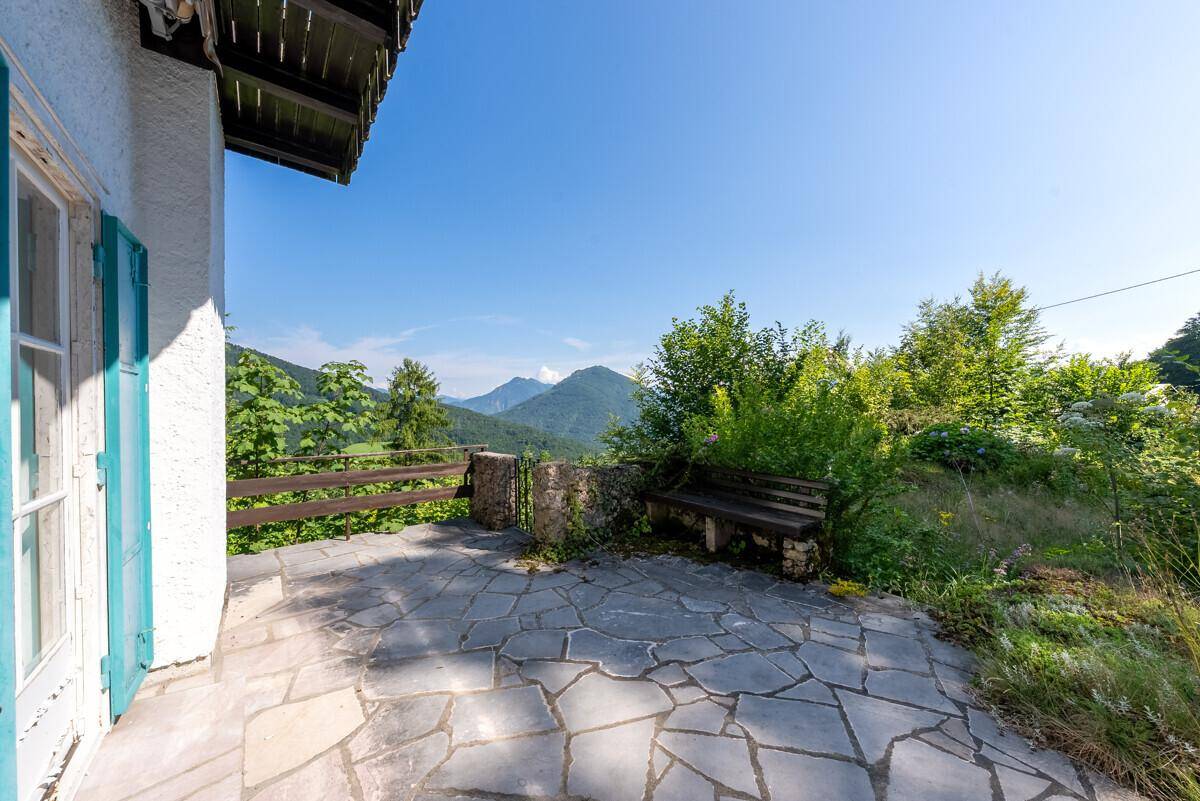 Gepflasterte Terrasse mit Steinplatten, Holzbank und weitem Blick auf die umliegende Berglandschaft.