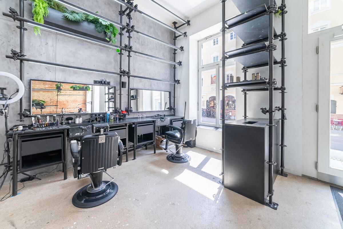 Arbeitsbereich in einem modernen Studio mit Friseurstühlen, Spiegeln, industriellen Regalen und großen Fenstern.