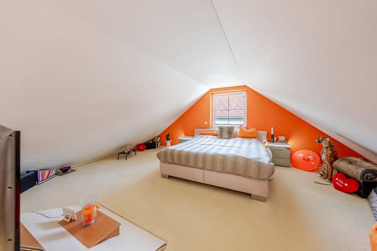 Schlafzimmer im Dachgeschoss mit Dachschräge, Fenster und farbenfroher Dekoration.