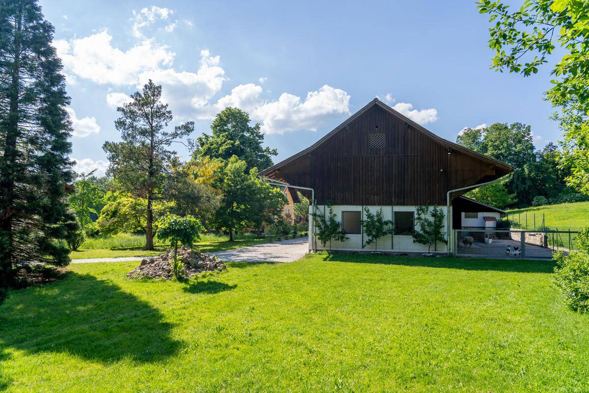 Ein ländliches Gebäude mit großem, gepflegtem Rasen und hohen Bäumen unter blauem Himmel.