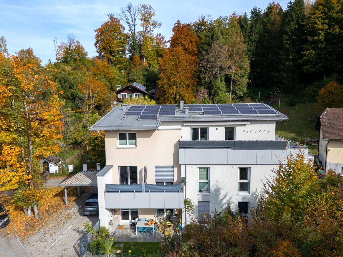 Luftaufnahme des Gebäudes mit Photovoltaikanlage auf dem Dach und Balkonen, umgeben von Herbstbäumen.