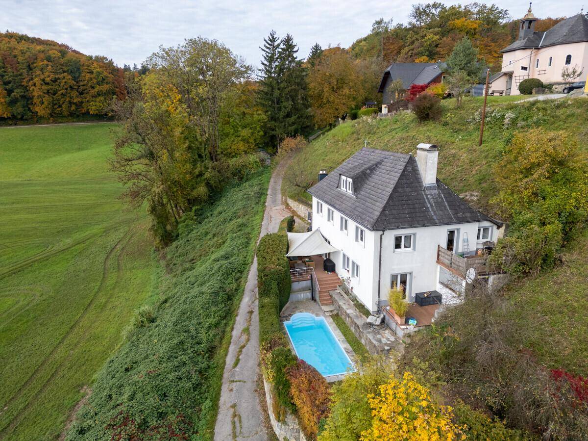 Luftaufnahme des Hauses mit Pool, umgeben von grünen Hängen und Bäumen.