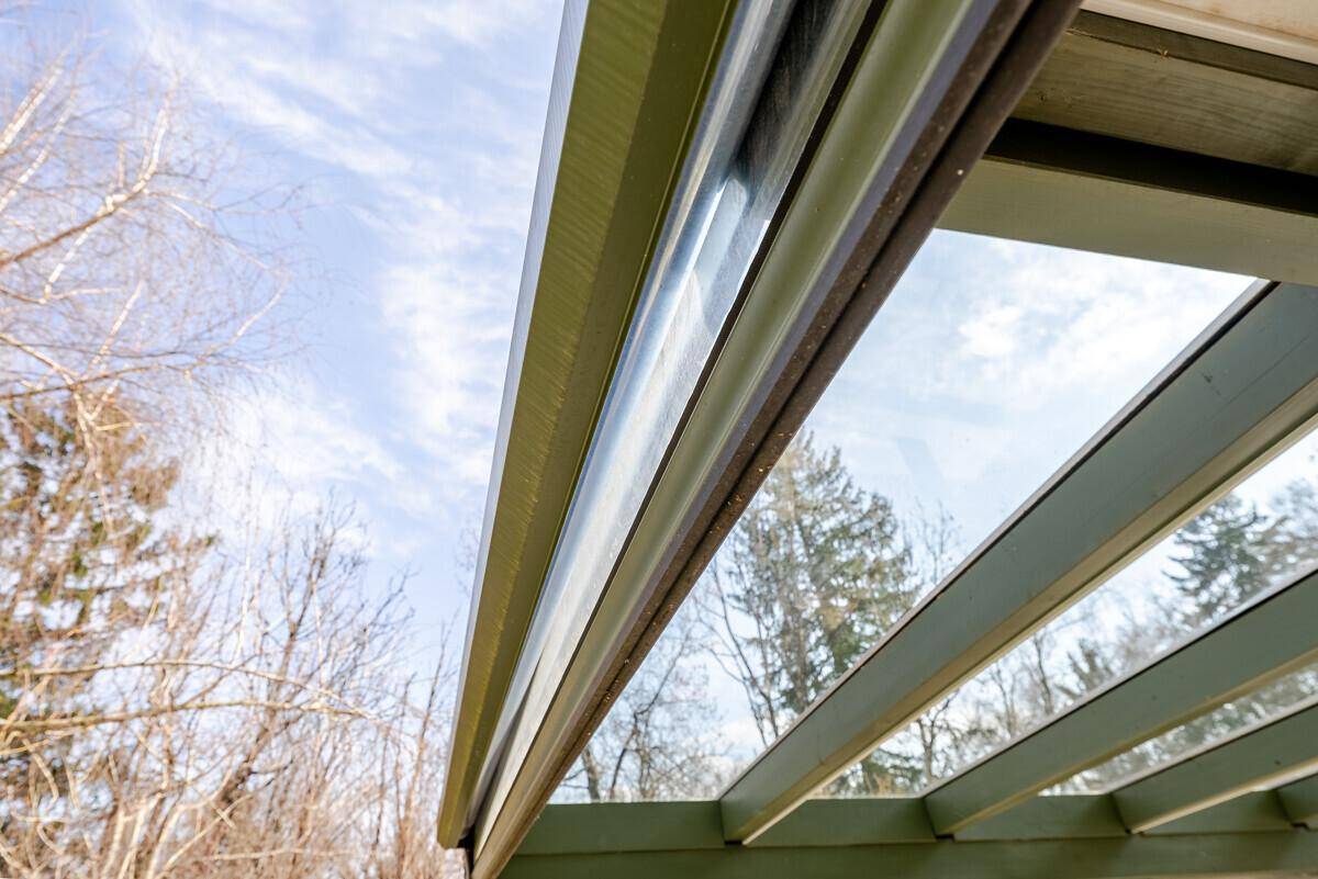 Detailansicht der Glasdachkonstruktion eines Wintergartens unter blauem Himmel.