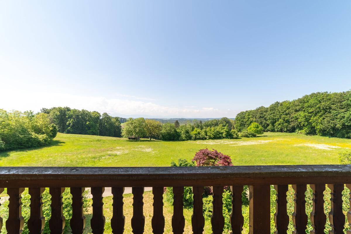 Weitläufiger Blick vom Balkon über grüne Wiesen und Wälder bis zum Horizont an einem sonnigen Tag.