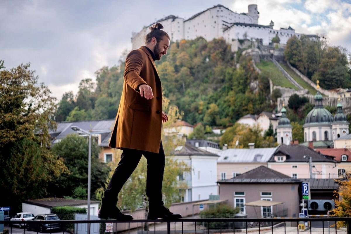Ein Mann balanciert auf einem Geländer mit malerischem Blick auf die Stadt Salzburg und die Festung Hohensalzburg.