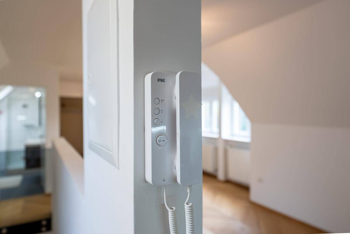 Gegensprechanlage an einer weißen Wand im Flur, mit Blick auf einen hellen Dachgeschossbereich.