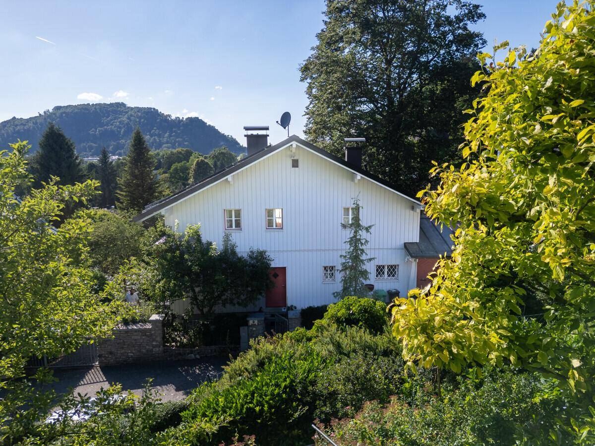 Rückansicht des Hauses mit weißer Holzfassade, umgeben von einem grünen Garten.