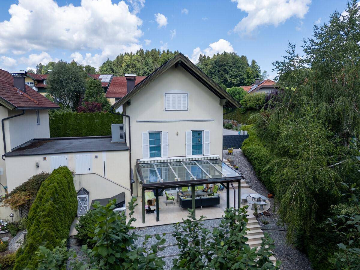 Rückansicht eines Hauses mit überdachter Terrasse, Garten und Blick auf die grüne Umgebung.