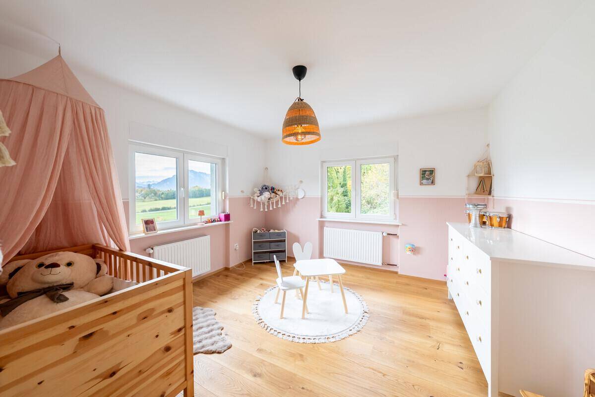 Helles Kinderzimmer mit Babybett, kleinem Tisch und rosa Akzenten, ideal für Kleinkinder.