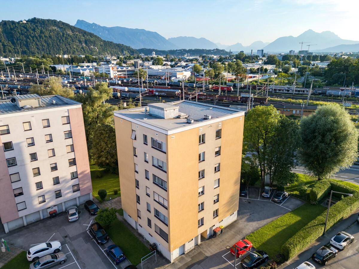 Luftaufnahme des Wohngebäudes mit umliegenden Parkplätzen und Blick auf die Berge.