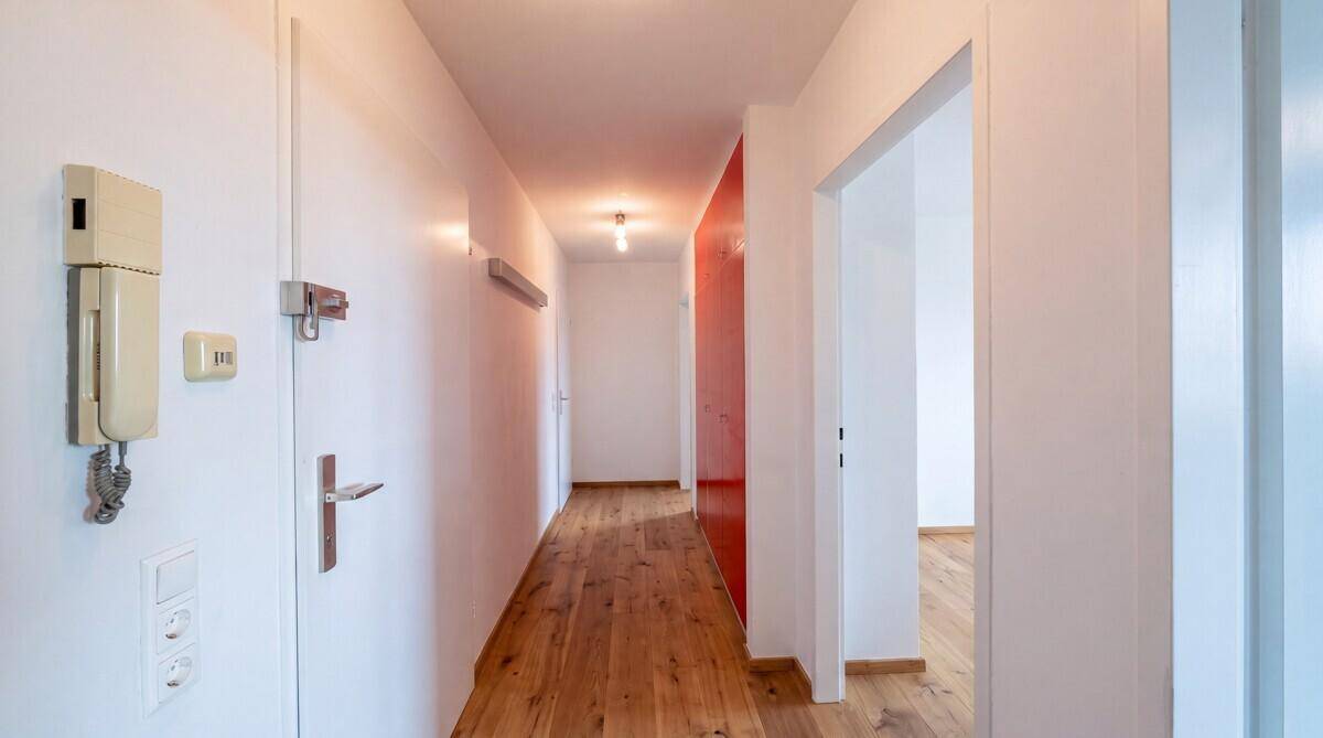 Heller Flur mit Holzboden und weiß gestrichenen Wänden, der zu den Zimmern führt.