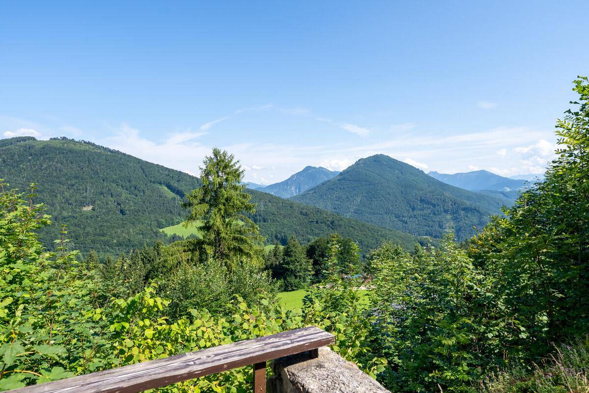 Weitblick von der Terrasse über grüne Täler und majestätische Berge unter klarem blauem Himmel.