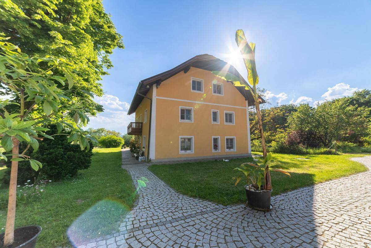 Gelbes Wohnhaus mit traditioneller Architektur, umgeben von gepflegtem Rasen und einem gepflasterten Weg.