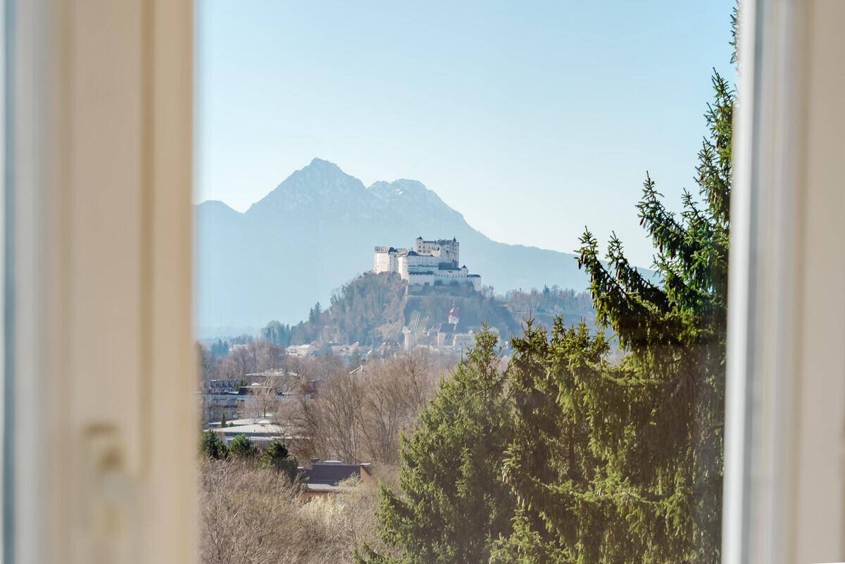 Panoramablick aus dem Fenster auf die Festung Hohensalzburg und die umliegende Berglandschaft.