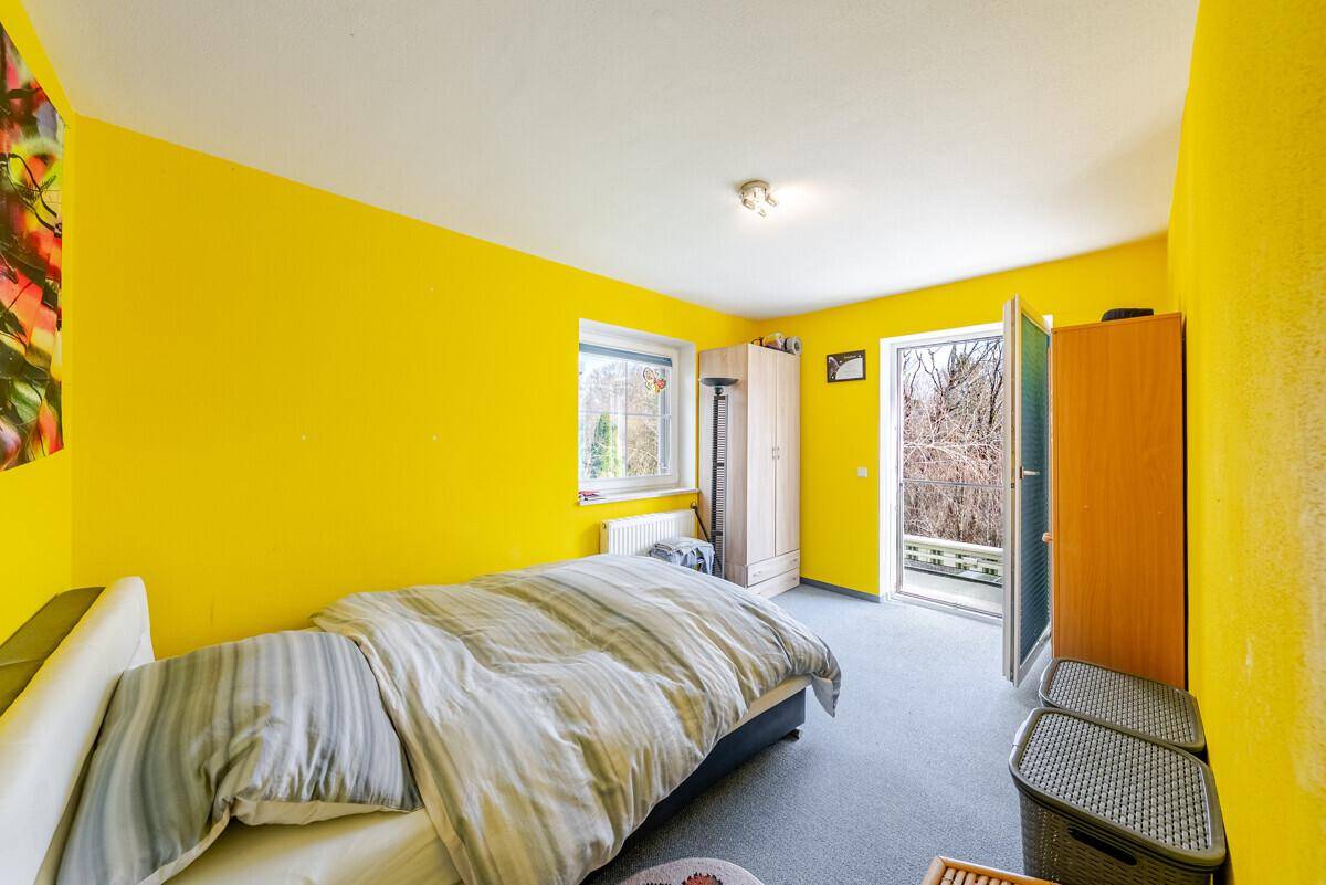 Helles Schlafzimmer mit gelben Wänden, Teppichboden und Zugang zu einem kleinen Balkon.