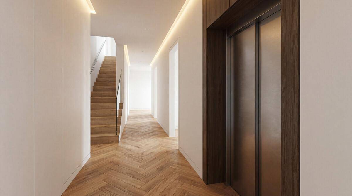 Heller Flur mit Holzparkettboden, moderner Beleuchtung und integriertem Aufzug sowie Treppenhaus.