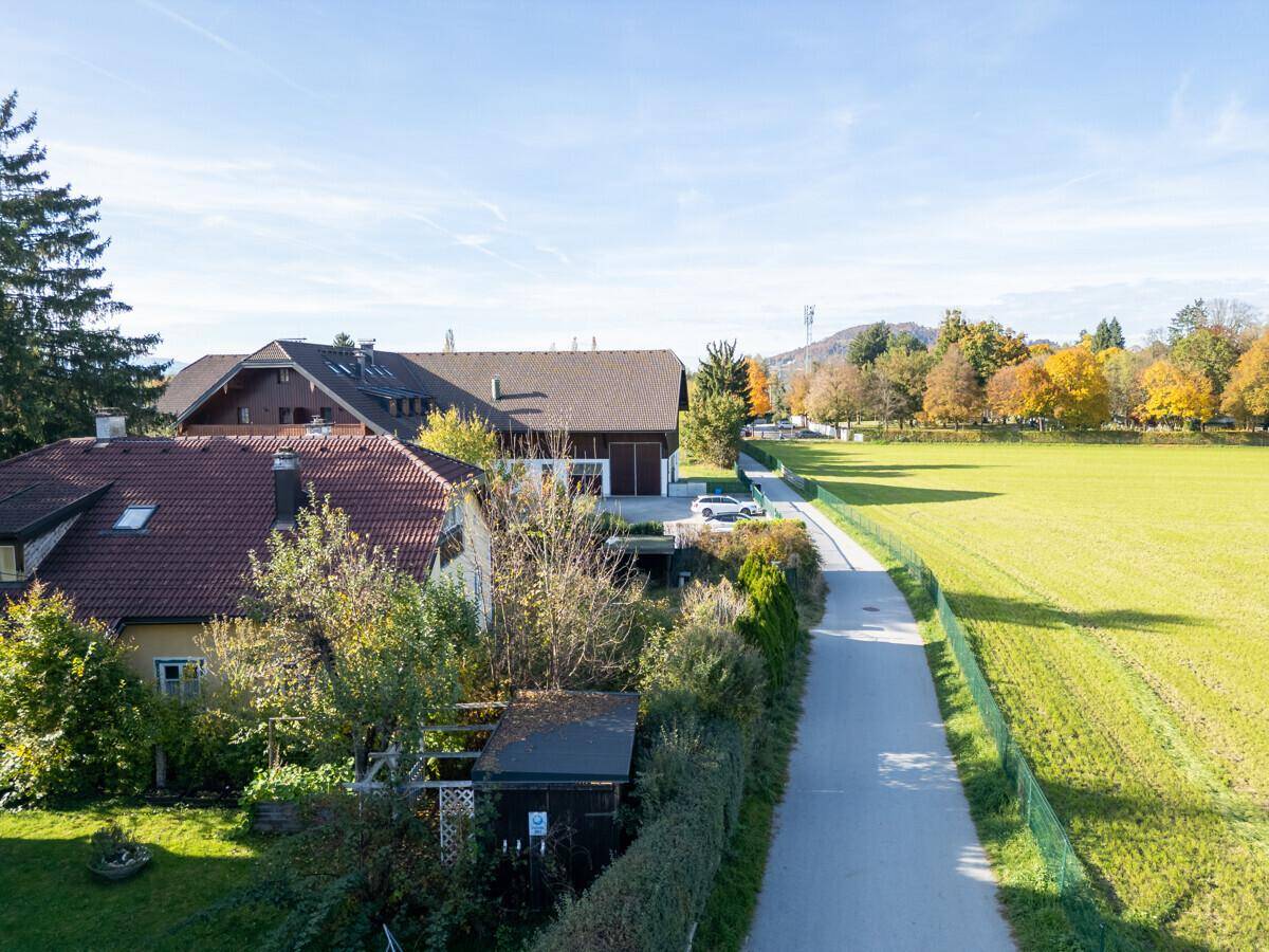 Luftaufnahme eines Hauses mit rotem Dach neben einem Feldweg und weiten grünen Feldern.