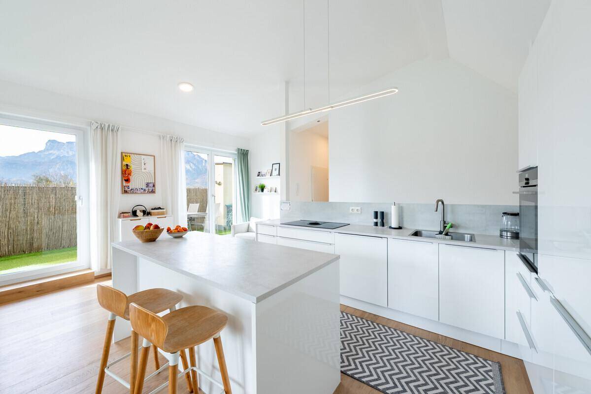 Moderne, helle Küche mit weißen Schränken, Kücheninsel und Blick auf die umliegende Berglandschaft.