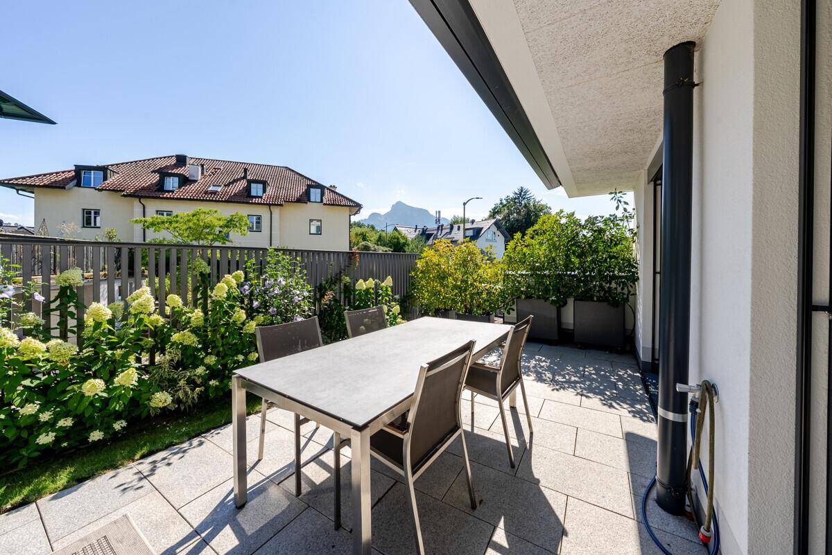 Gemütliche Terrasse mit Esstisch und Stühlen, umgeben von blühenden Pflanzen und mit Bergblick.