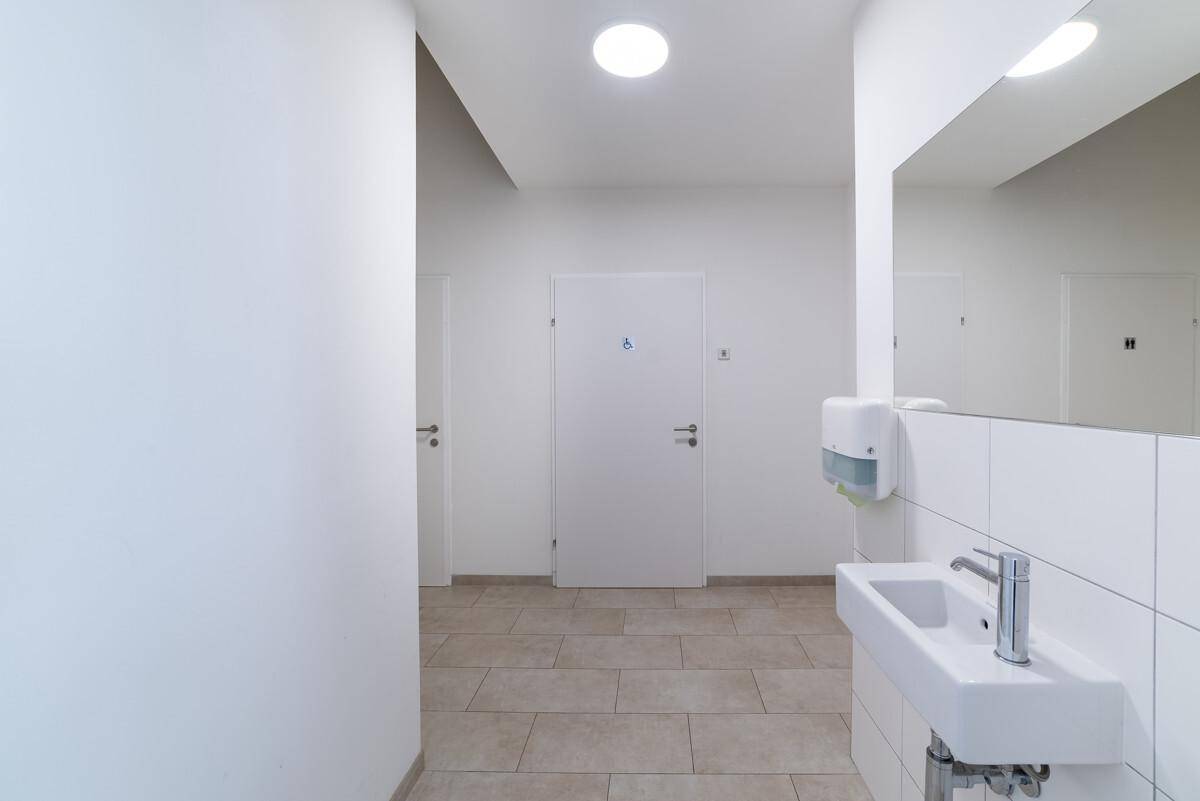 Heller Flur mit Waschbecken und Spiegel, der zu weiteren Räumen führt, mit barrierefreier Tür.
