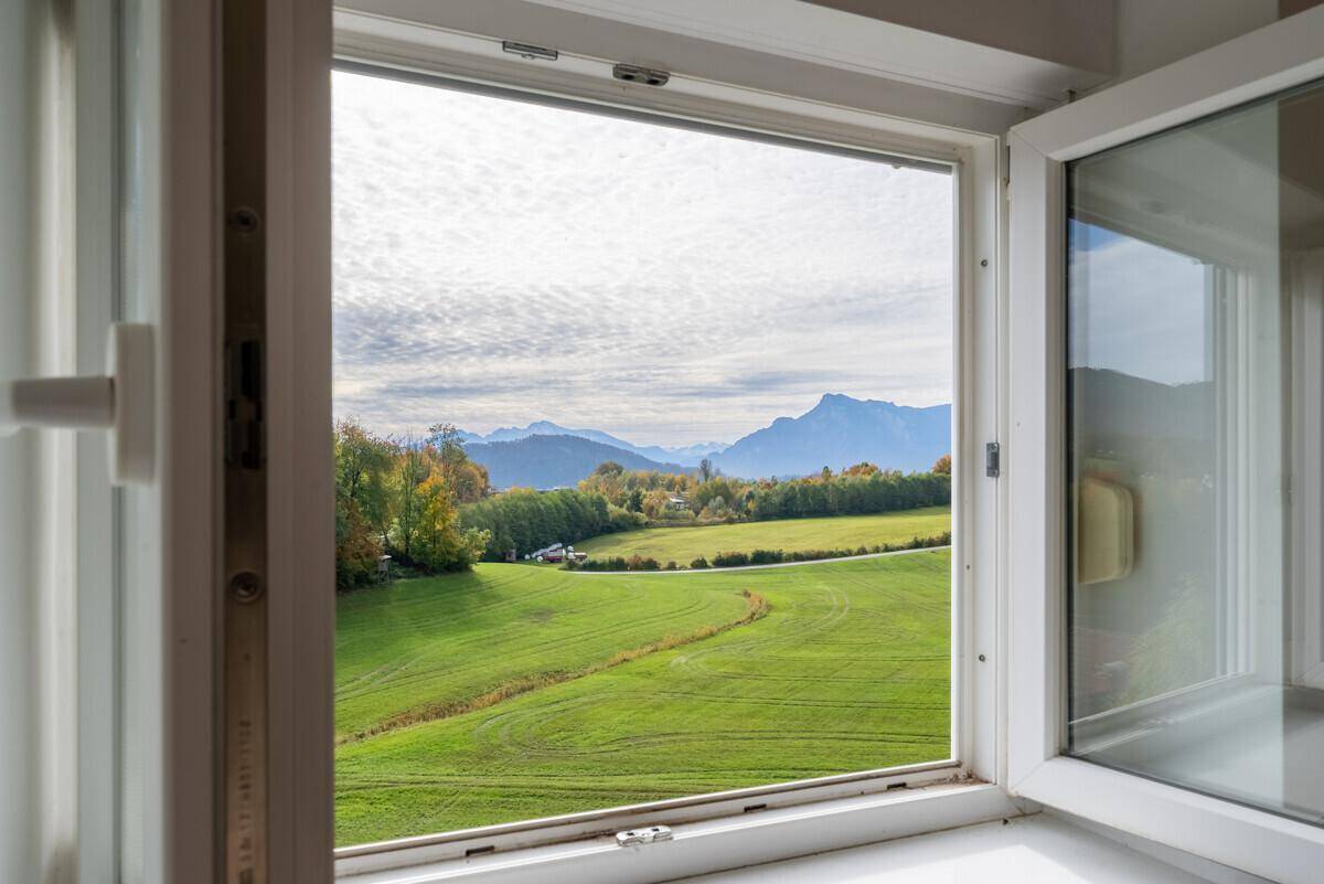 Offenes Fenster mit weitem Blick auf die grüne Landschaft und die majestätischen Berge.