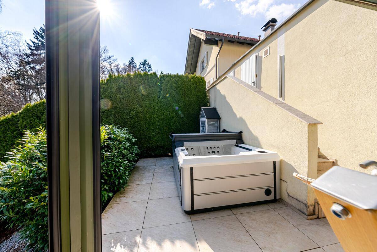 Kleine geflieste Terrasse mit Whirlpool und Hecke, ideal zum Entspannen im Freien.