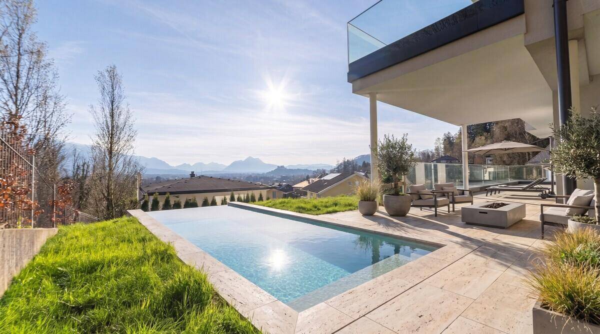 Sonniger Außenbereich mit Infinity-Pool, großer Terrasse und Panoramablick auf die Berge.