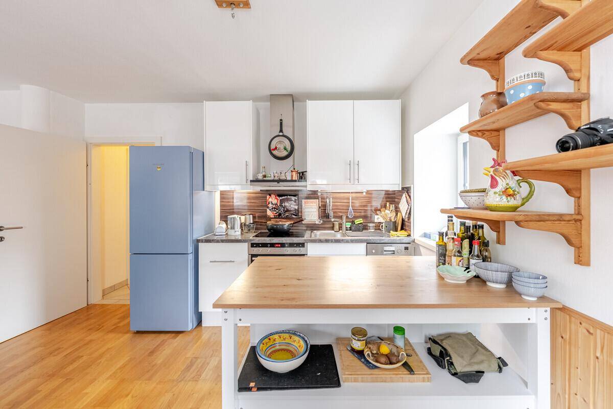 Helle Einbauküche mit weißen Fronten, Holzdetails und einem auffälligen blauen Kühlschrank.