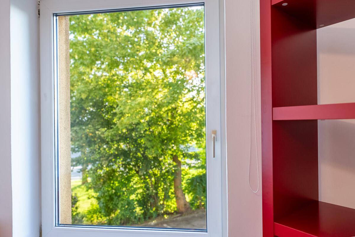 Fenster mit Blick auf üppiges Grün und einem roten Regal im Innenraum.