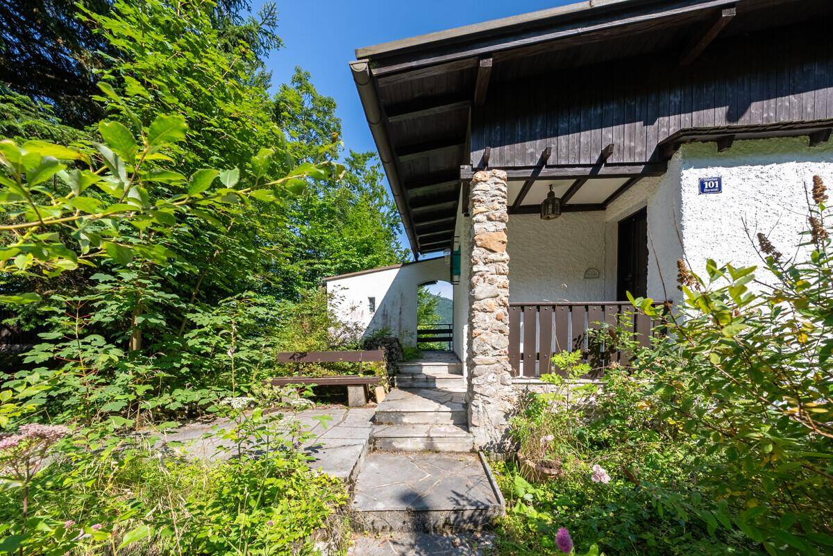 Eingangsbereich des Hauses mit überdachter Veranda, Steinpfeiler und einer rustikalen Holzbank.