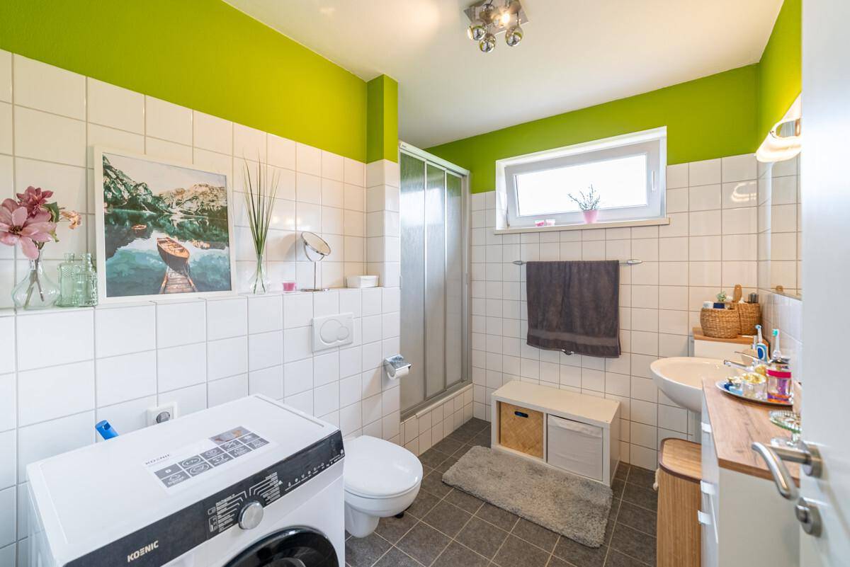 Helles Badezimmer mit grünen Akzentwänden, Dusche, WC und Waschmaschine.