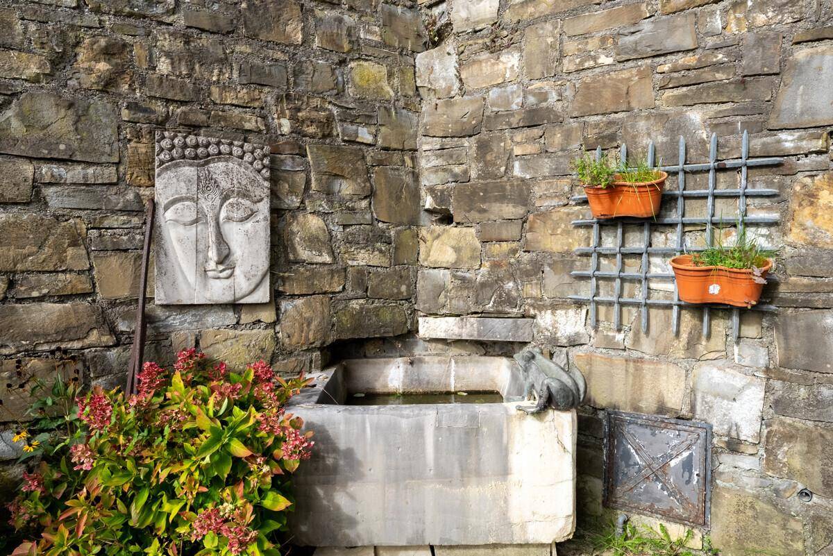 Dekorative Steinmauer mit Buddha-Relief und einem kleinen Wasserbecken im Gartenbereich.