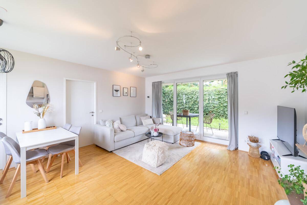 Gemütlicher Wohn- und Essbereich mit hellem Sofa, Esstisch und Blick ins Grüne.