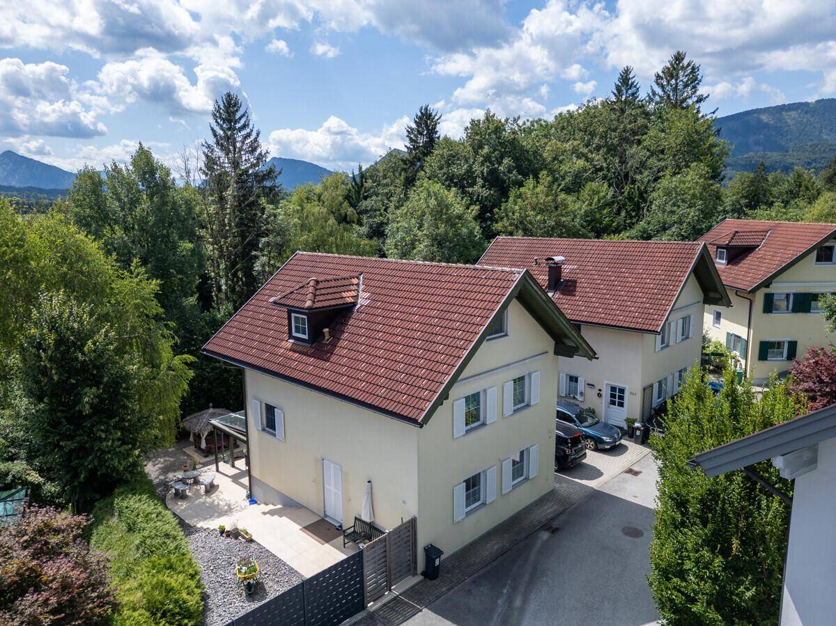 Ansicht eines Einfamilienhauses mit hellgelber Fassade, roten Ziegeldächern und grüner Umgebung.