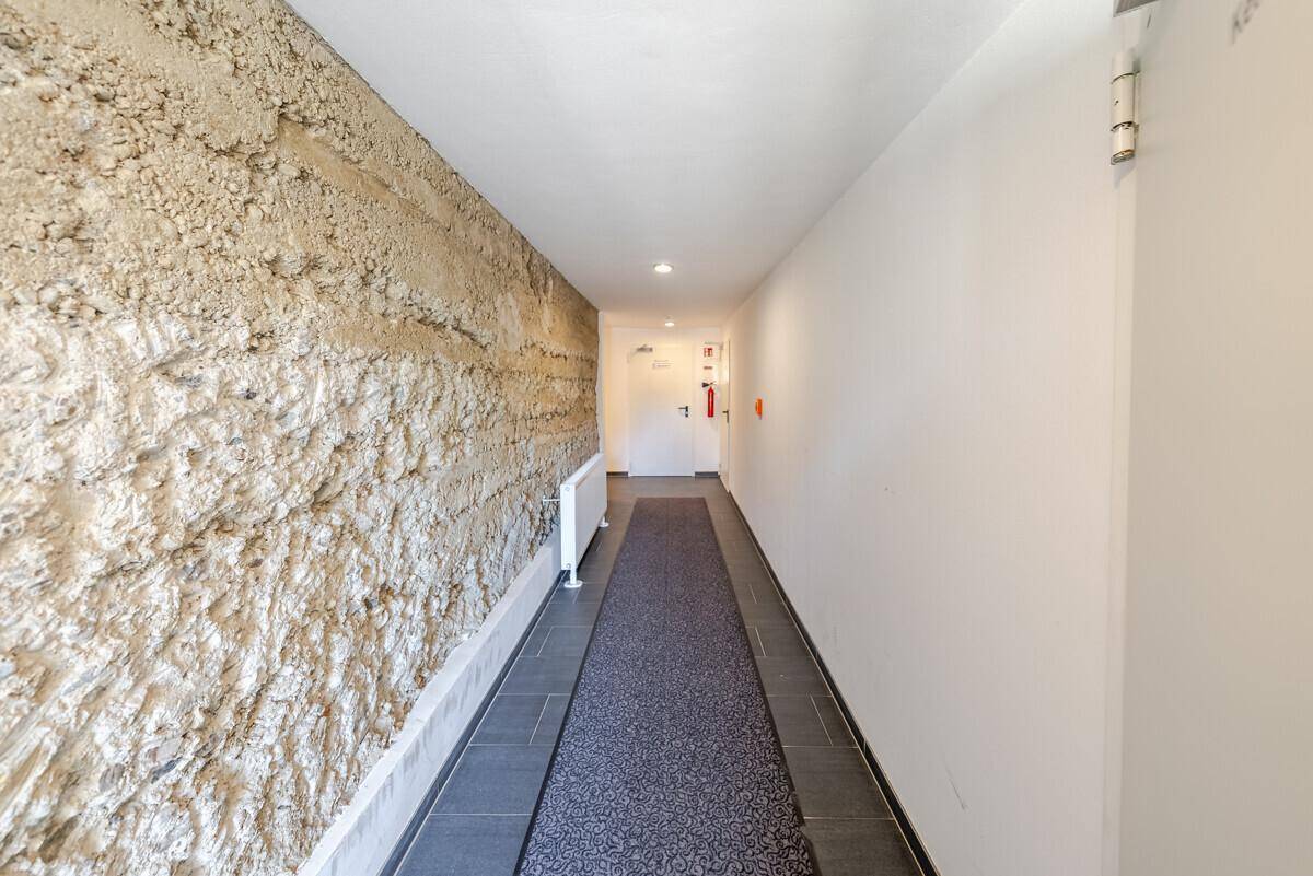 Gemeinschaftsflur mit strukturierter Wand und Fliesenboden, der zu den Wohneinheiten führt.