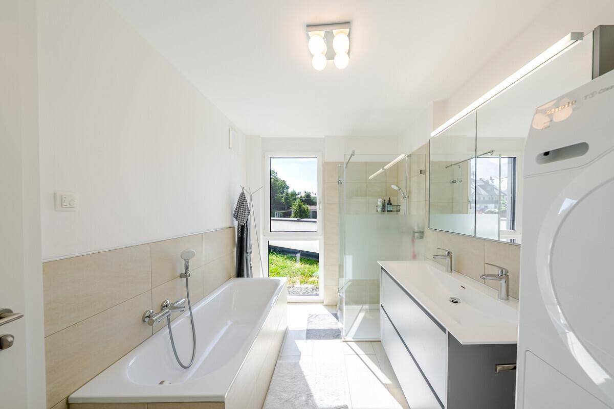 Modernes Badezimmer mit Badewanne, begehbarer Dusche, Doppelwaschbecken und Fenster für Tageslicht.
